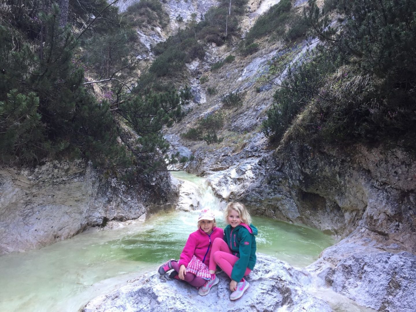 Wandern mit Kindern macht Spass! Hier sitzen zwei entzückende Mädchen auf zwei Steinen inmitten einer Klamm und strahlen in die Kamera